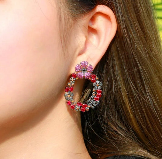 A close-up of a womans ear wearing DiamondVeneer Fashion Flower Circle Zirconite Cubic Zirconia Earrings (826E06), featuring pink flowers and circular hoops set with sparkling pink and silver gemstones.