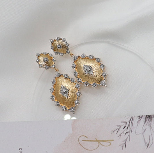 DiamondVeneer Fashions Zirconite inspired Italian satin Door Knocker Earrings (831E102) feature gold and silver leaf-like shapes with pavé stones, beautifully displayed on white fabric beside a floral card.