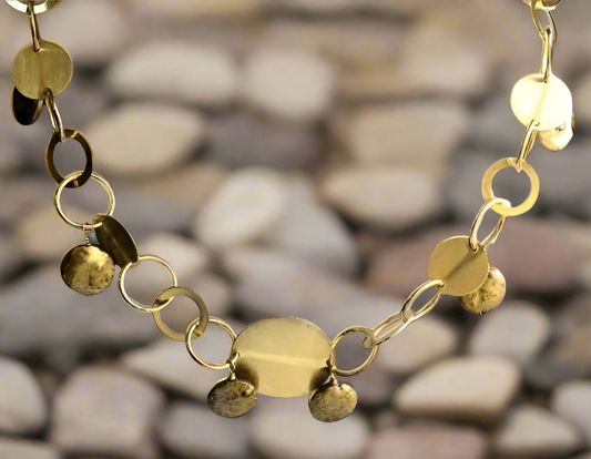 A close-up of the DiamondVeneer Fashion O links Gold Coin Pearls Necklace (STN230), featuring handcrafted gold oval links and discs with freshwater coin pearls, displayed on smooth, light-colored stones. Final Sale.