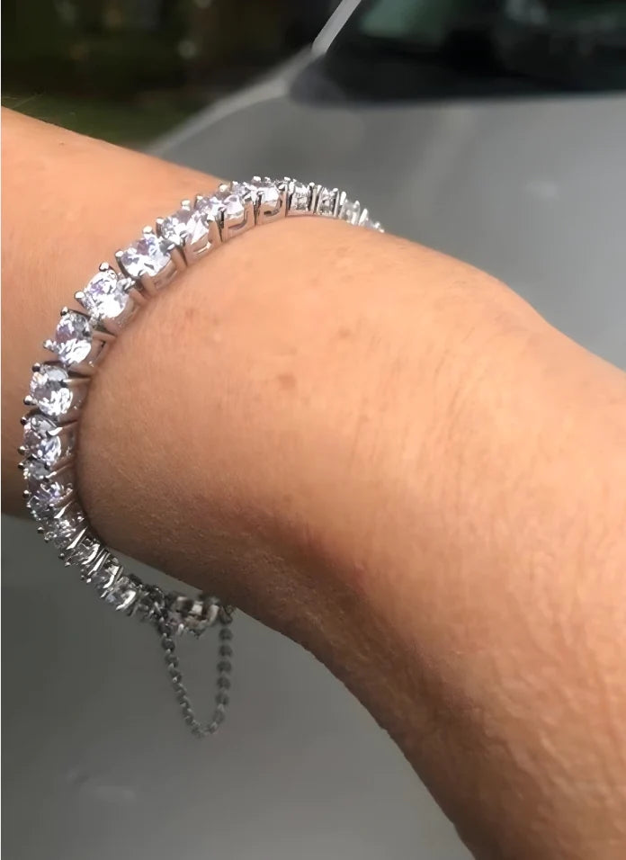 Woman's wrist wearing diamond veneer simulated diamond tennis bracelet with dangling safety chain.