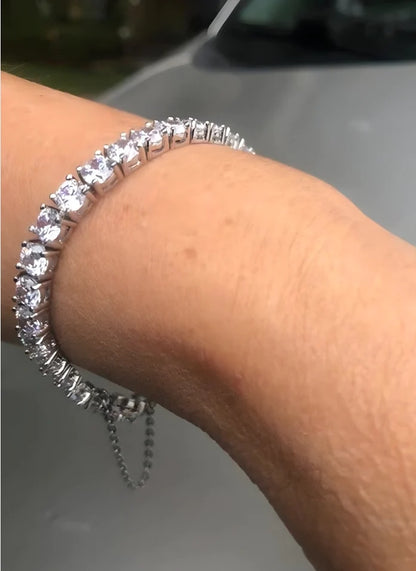 Woman's wrist wearing diamond veneer simulated diamond tennis bracelet with dangling safety chain.
