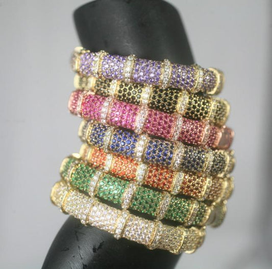 A set of six DiamondVeneer Fashion Face-off Zirconite Crystal Pave Hinged Bangle Bracelets (698B10C) in purple, pink, yellow, orange, green, and white, elegantly displayed on a black stand.