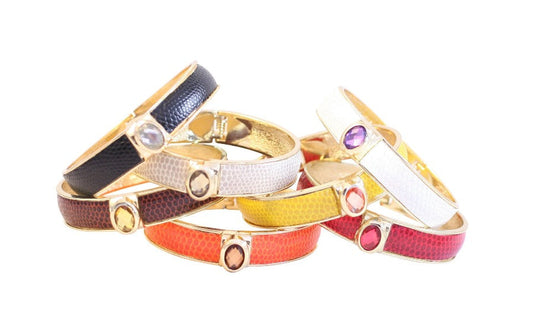 A scattered pile of DiamondVeneer Fashion Zirconite Oval Jeweled Leather Hinged Bracelet Bangles (629B82033) features gold accents, oval gemstones, and red, orange, yellow, white, and black textured bands on a white background.