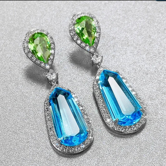 DiamondVeneer Fashions Aqua Blue Cubic Zirconia Earrings (Zirconite.826E1074) feature green teardrop gems and bold blue geometric stones, both accented by clear crystals, beautifully displayed on a shimmering silver surface.