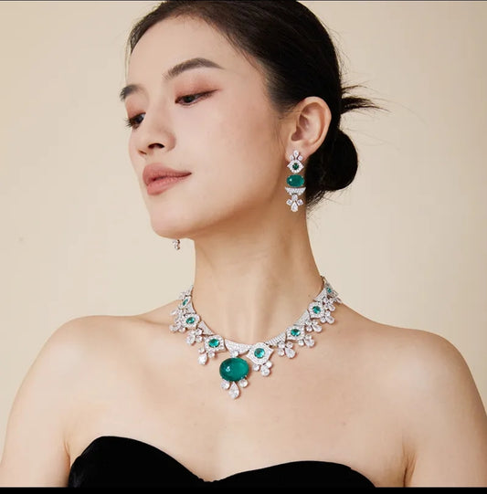 Woman in black top showcases Zirconmania emerald cabochon necklace & earrings set with zirconite, on beige background.
