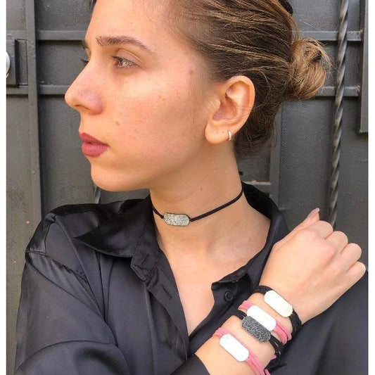 A woman in a black shirt with her hair in a low bun wears the DiamondVeneer Fashion Trendy Fully Paved Zirconite Cubic Zirconia ID Bracelet/Choker (655B807), styled with matching stone bracelets and choker accents.
